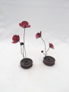 una flor de forja sujeta a una rueda de metal, llamada amapola rueda metal.