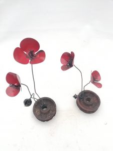 una flor de forja sujeta a una rueda de metal, llamada amapola rueda metal.