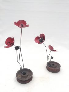una flor de forja sujeta a una rueda de metal, llamada amapola rueda metal.