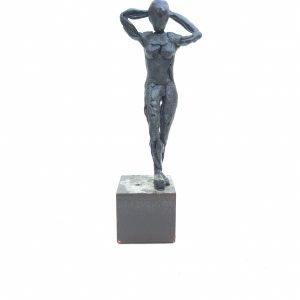 Escultura de una figura femenina modelada en resina epoxi en posición de pie y con los brazos descansando detrás de la cabeza. La figura está en una base de acero macizo a modo de pedestal.
