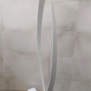 Escultura abstracta de metal con dos piezas curvadas blancas, formando un óvalo en posición vertical, sobre una base rectangular de metal oxidado y barnizado.