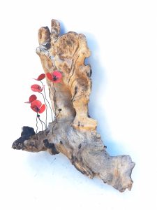 Escultura de un tronco natural con un conjunto de amapolas rojas de metal alojadas en ella