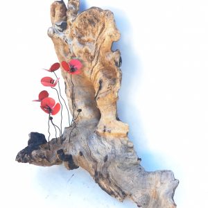 Escultura de un tronco natural con un conjunto de amapolas rojas de metal alojadas en ella